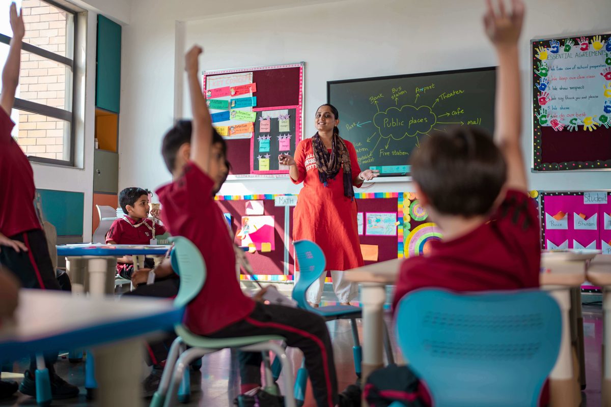 Teacher leading a lesson as students raise their hands in a Geneva Liberal School classroom