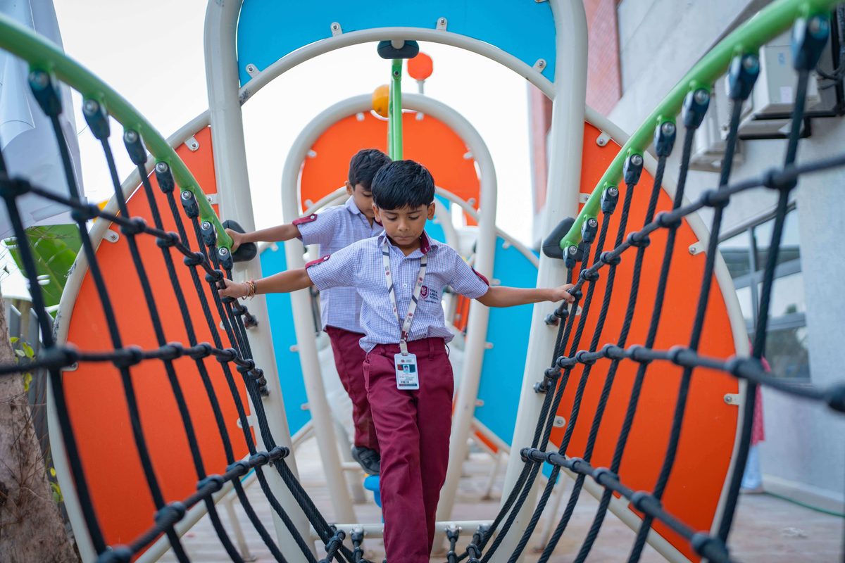Students crossing the rope bridge on the campus play structure